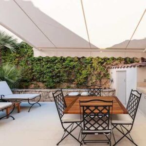 Covered patio with verdant wall, wooden table, iron chairs, and loungers