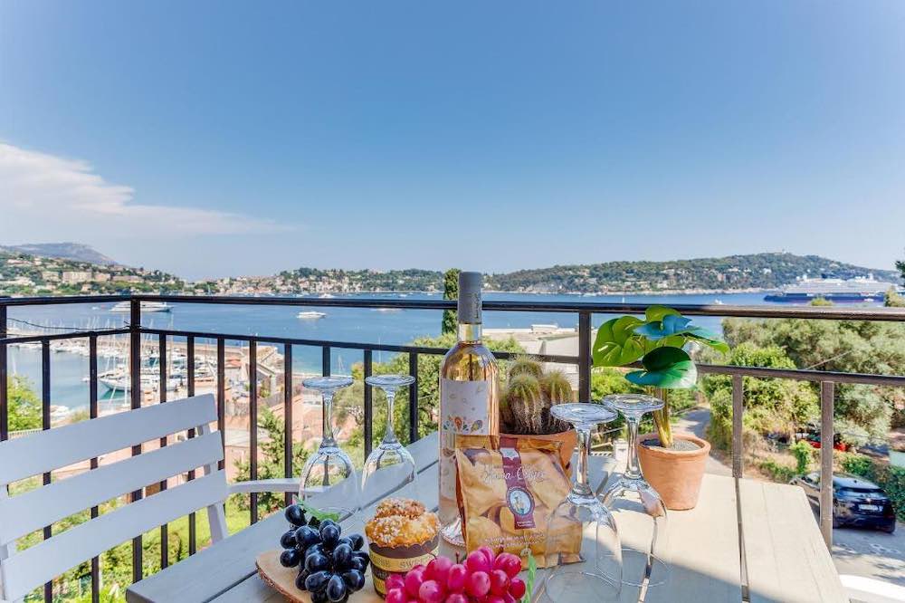 Terrace table set with fingerfoods and a bottle of wine overlooking the Rade de Villefranche-sur-Mer